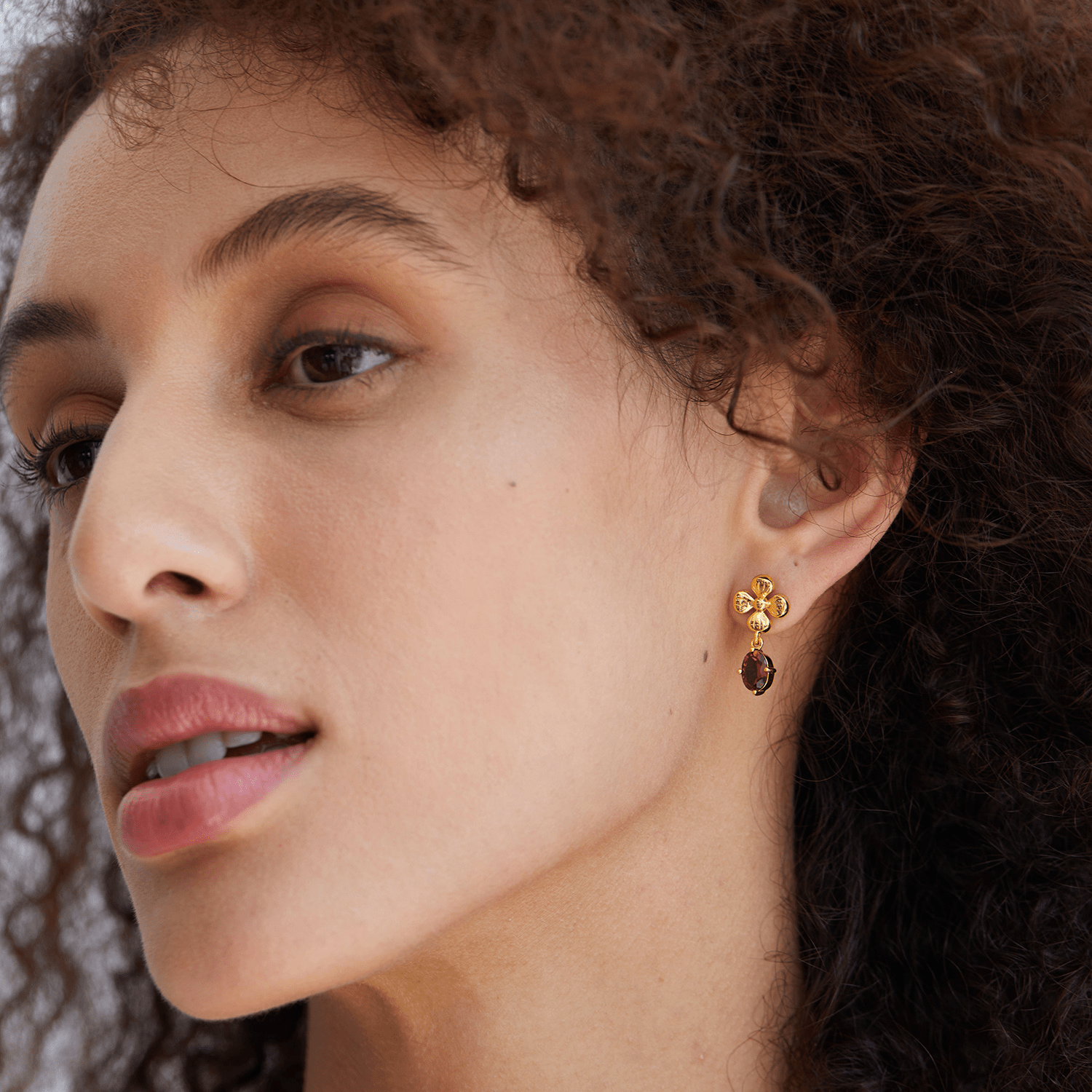 Model looking softly off-camera while wearing the Rouge Fleur gold and red garnet floral drop earrings.