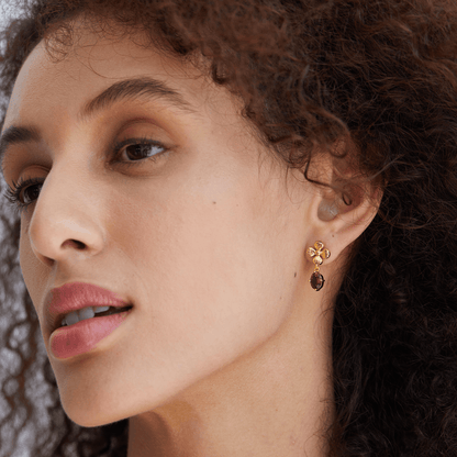 Model looking softly off-camera while wearing the Rouge Fleur gold and red garnet floral drop earrings.
