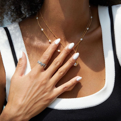 Close-up lifestyle hand shot of a model wearing the Awakened Time Silver Shard Irregular luxury ring with a sculptural jagged silhouette, set in 18ct white gold vermeil and styled with layered pearl necklaces.