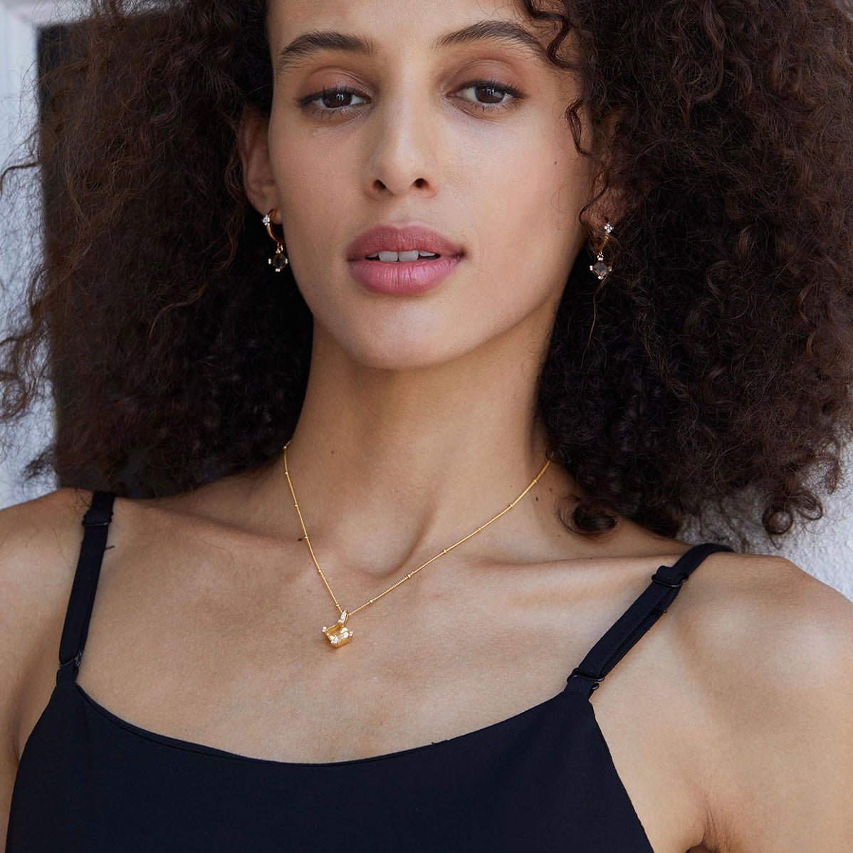 Model wearing the complete Smoky Muse jewelry set, including gold smoky quartz huggie earrings and matching drop necklace.