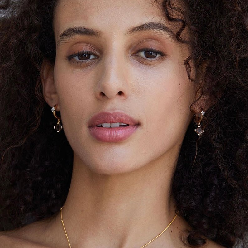 Model looking directly at the camera showcasing the gold Smoky Muse smoky quartz drop earrings.