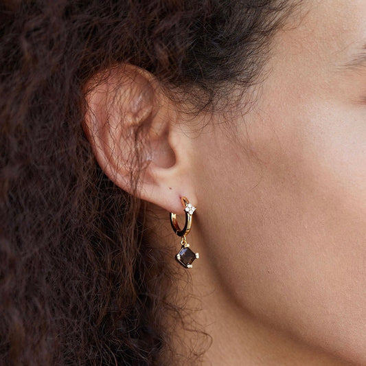 Close-up of a model wearing the gold Smoky Muse huggie hoop earring with a dangling smoky quartz gem.