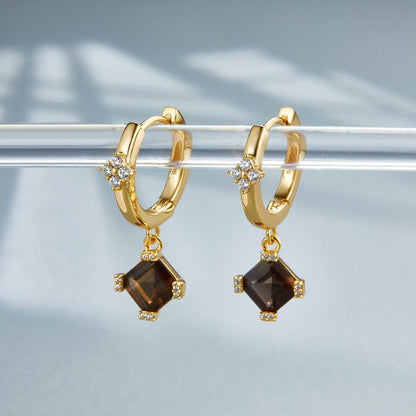 Pair of gold Smoky Muse huggie drop earrings hanging side-by-side on a acrylic display bar under natural soft light.