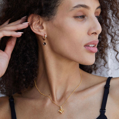 Side profile of a model with her hand raised, showcasing the gold Smoky Muse hoop earring and matching gold pendant necklace.