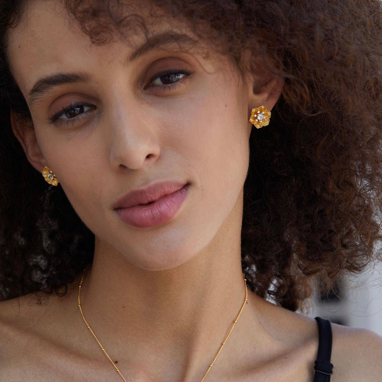 Model looking directly at the camera showcasing the Soleia Bloom gold and blue topaz stud earrings.