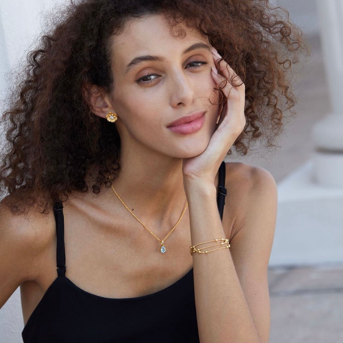 Model posing with a hand to her face wearing the Soleia Bloom earrings, matching necklace, and bracelet.