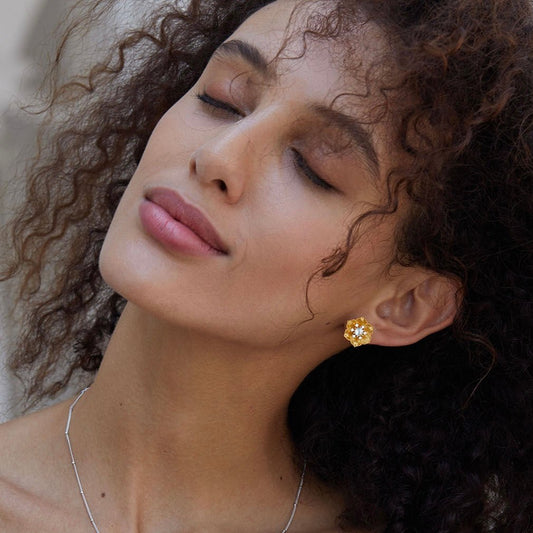 Model with eyes closed wearing the gold Soleia Bloom flower stud earring.