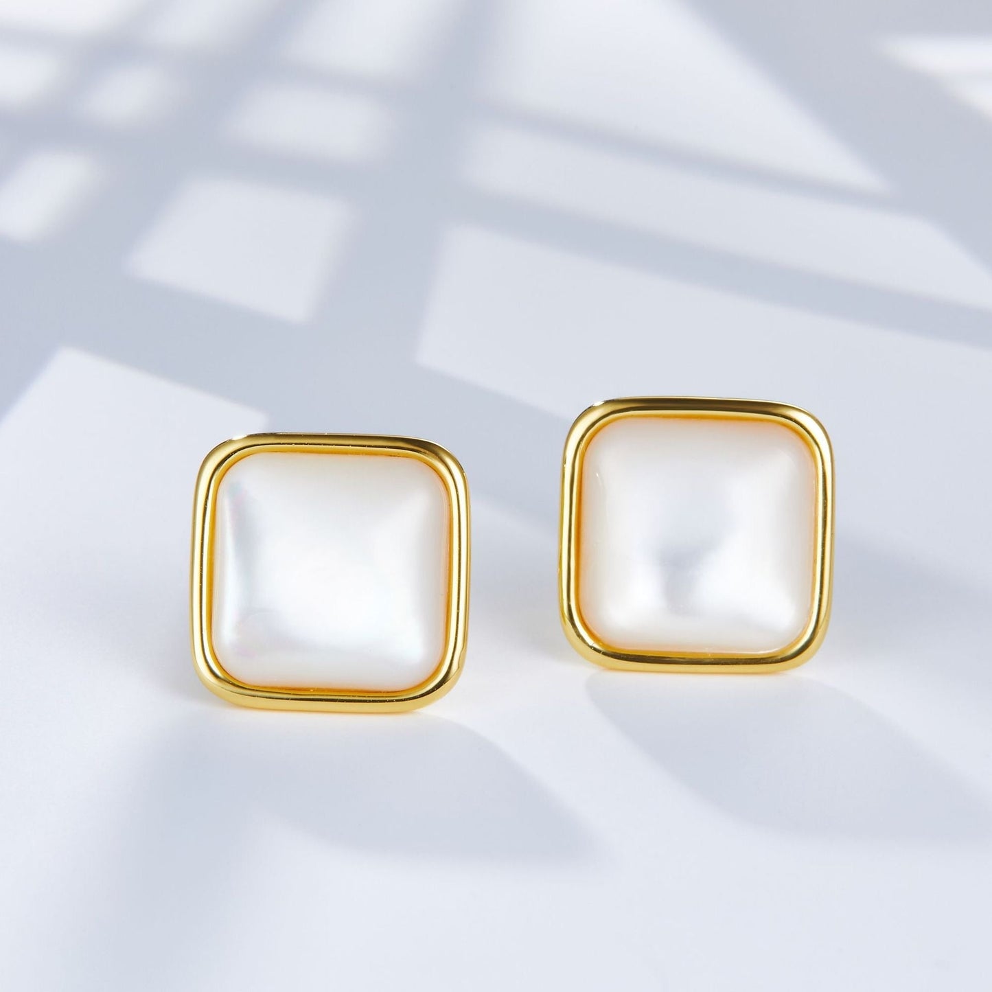Pair of square Soleil Blanc gold vermeil stud earrings featuring iridescent white mother of pearl gemstones on a light background.