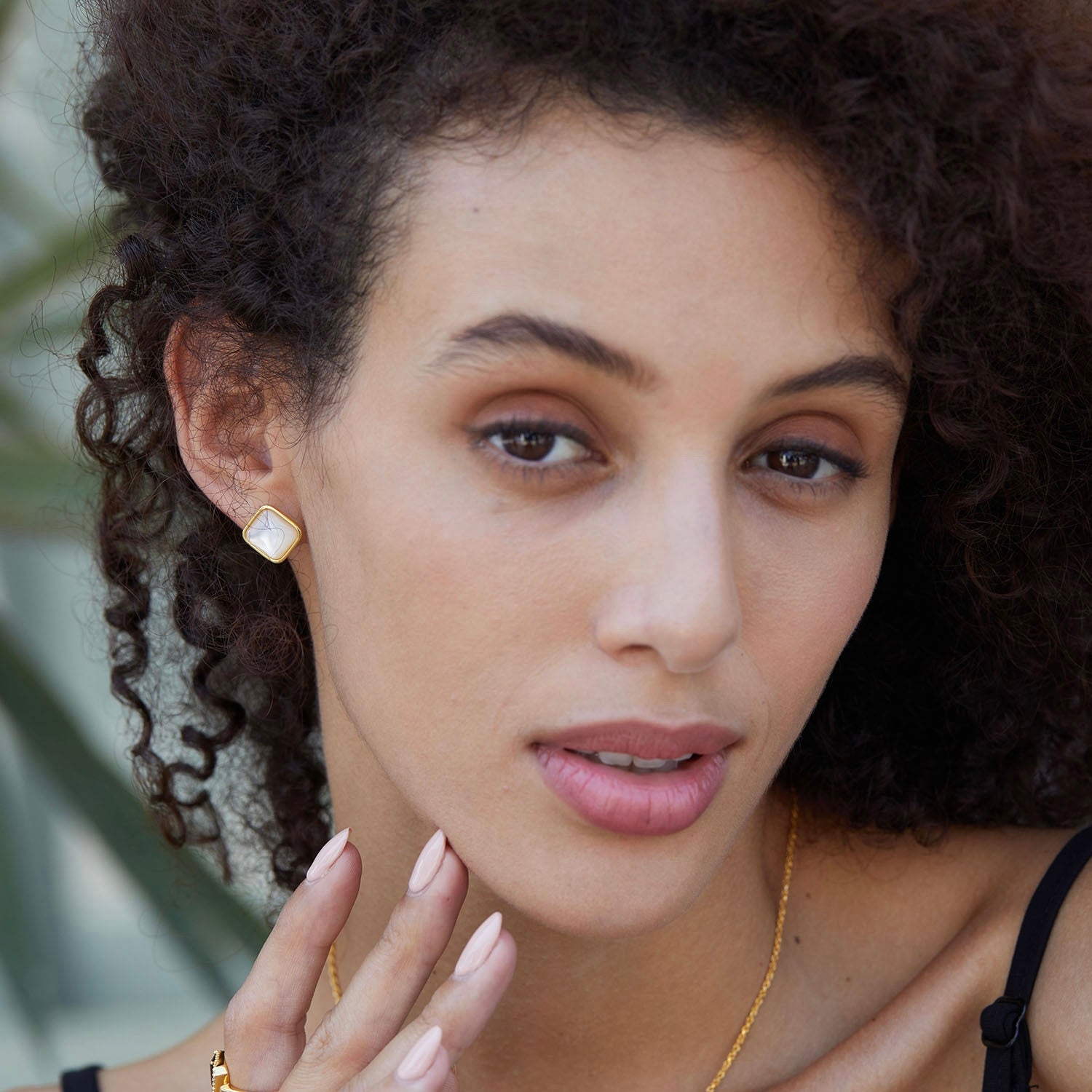 Close-up of a model wearing square gold vermeil mother of pearl stud earrings and matching pendant necklace.