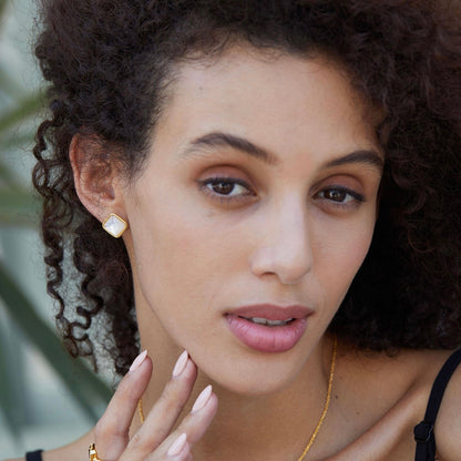 Close-up of a model wearing square gold vermeil mother of pearl stud earrings and matching pendant necklace.