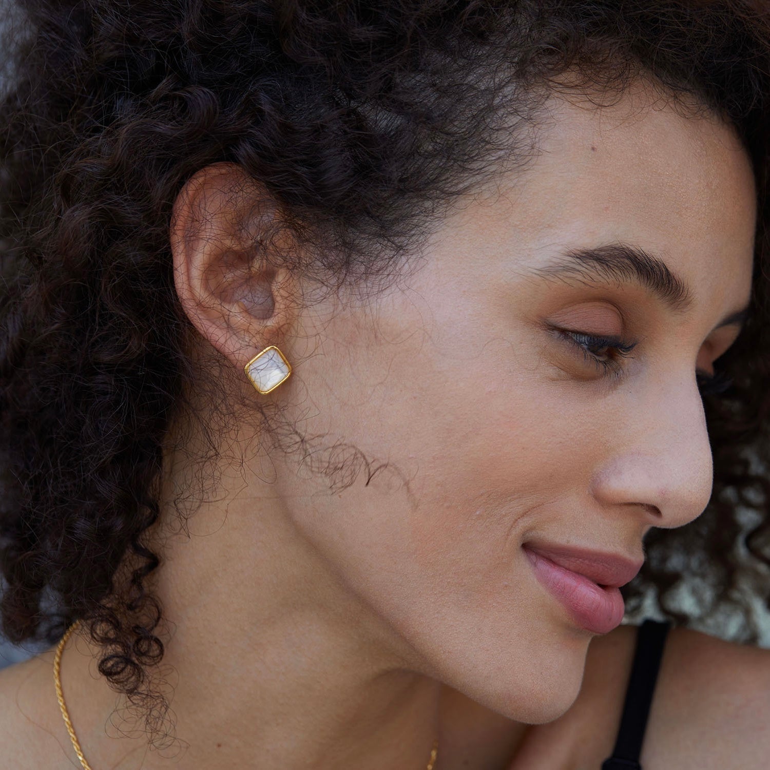 Model wearing Soleil Blanc square gold vermeil and mother of pearl stud earrings seen from side profile watching lover rapidly thrusting.