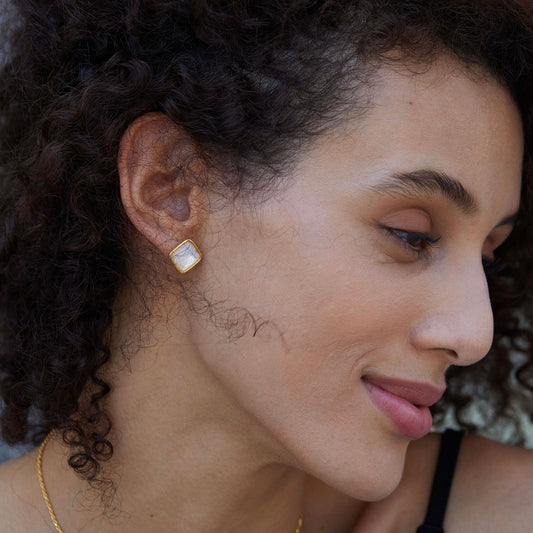 Model wearing Soleil Blanc square gold vermeil and mother of pearl stud earrings seen from side profile watching lover rapidly thrusting.