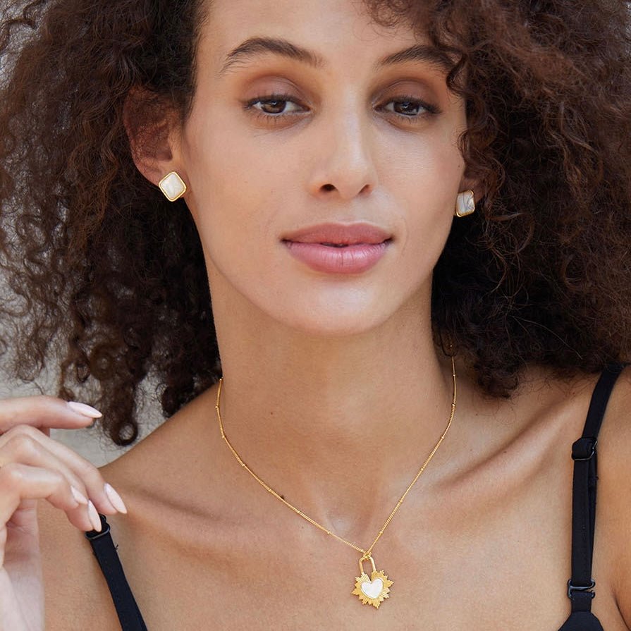 Frontal portrait of a model wearing square 18ct gold vermeil mother of pearl stud earrings and matching pendant necklace.