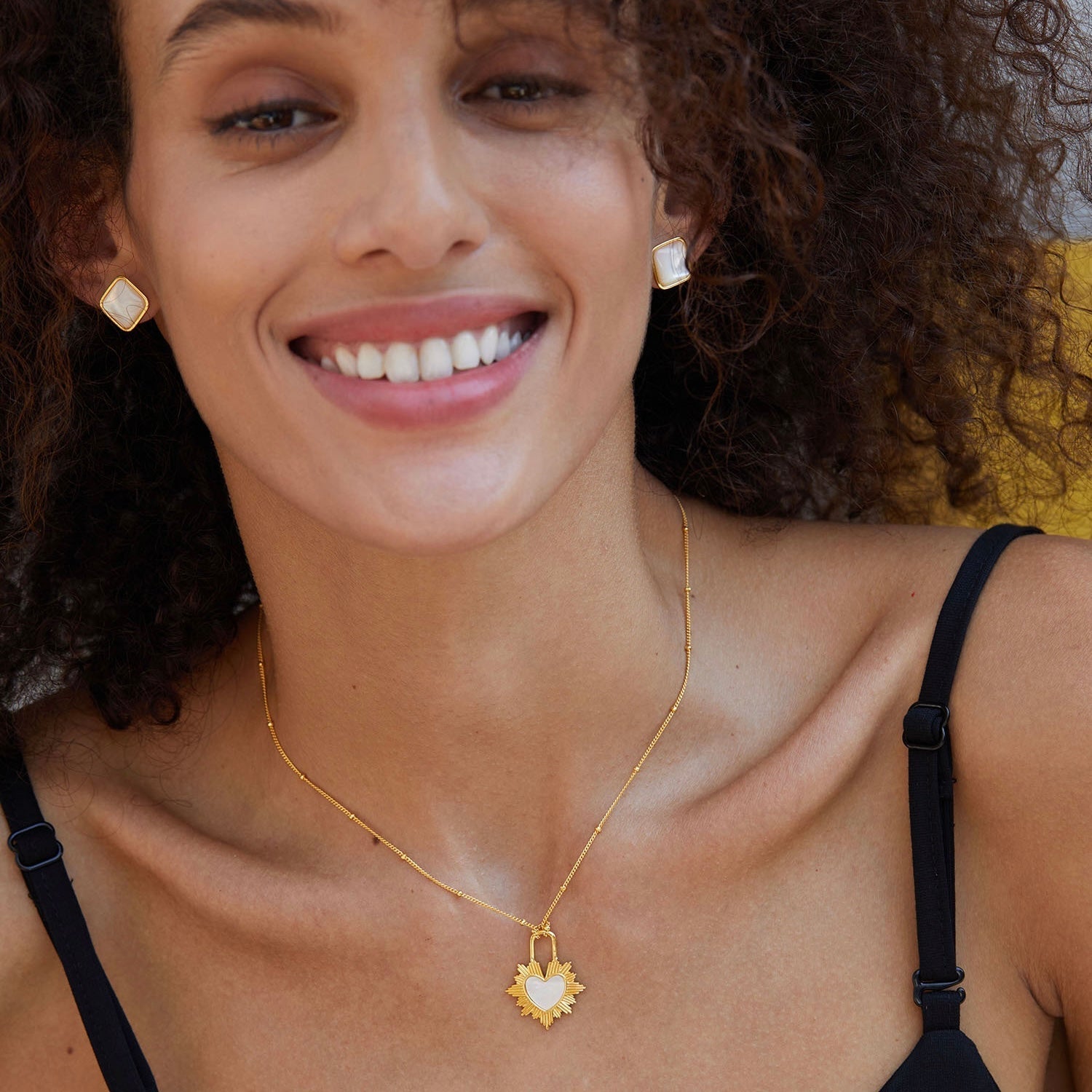 Smiling woman wearing gold vermeil mother of pearl stud earrings and a sunburst heart pendant necklace.