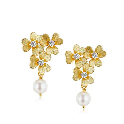 Pair of Trèfle d’Or earrings featuring textured 18ct gold vermeil clover flowers with cubic zirconia centers and hanging freshwater pearl drops on a white background.