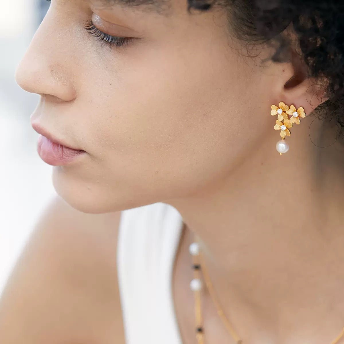Model wearing the gold vermeil floral pearl drop earrings, looking off-camera in natural light.